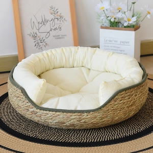Handwoven straw cat bed with green trim and plush white cushion on a decorative rug