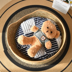 Detail shot of a hand-woven natural seagrass cat bed with a striped cushion and teddy bear