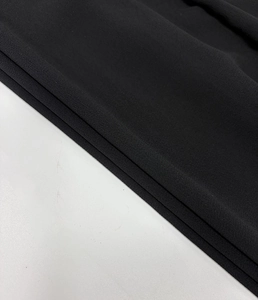 Detailed close-up of high-density black crepe fabric with fine granular texture and drape