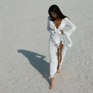 Detail of white beach cover-up featuring ruffled V-neck and flowing high-slit design