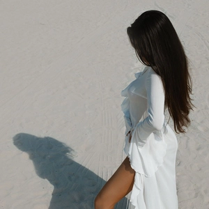 Close-up of white long-sleeved dress with ruffle trims and side slit on sandy beach