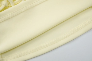 Detail of sewing edges and thin straps on a slim fit light yellow halter top