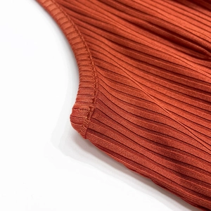 Detailed close-up of stitching on rust red ribbed knit fabric with soft elastic texture
