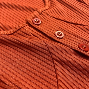 Close-up of ribbed knit texture and three-button neckline on a burnt orange summer dress