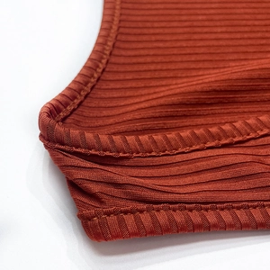 Detailed macro view of the rust-colored ribbed knit fabric with precise overlock stitching