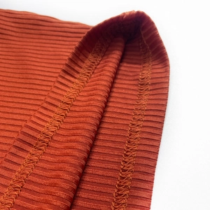 Detailed view of rust red ribbed knit fabric with professional overlock stitching detail