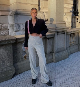 Dettaglio di un blazer corto nero abbinato a pantaloni larghi metallizzati argento al sole