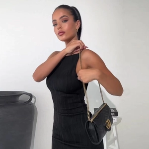 Détail de la robe moulante noire avec texture plissée et sac à boucle dorée élégante