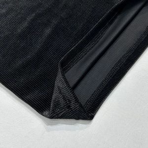 Detail van zwarte corduroy stof met fijne ribstructuur en een nette zoomafwerking