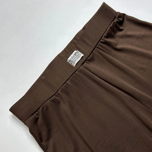 Detailed close-up of dark brown trousers with wide elastic waistband and decorative label