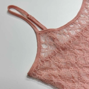 Détail de caraco en dentelle rose montrant des motifs floraux et des bretelles fines