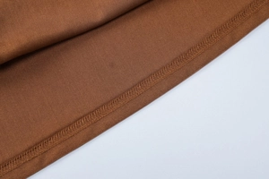 Gros plan détaillé montrant la couture surjetée sur l'ourlet de la robe marron ambre