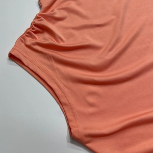 Detail of coral orange elastic fabric showing flat-locked stitching and side ruching