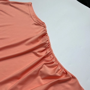 Detail of coral sleeveless dress featuring side ruched design and shiny knit fabric