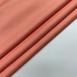 Detailed close-up of coral pink knitted fabric texture with vertical ribbing pattern