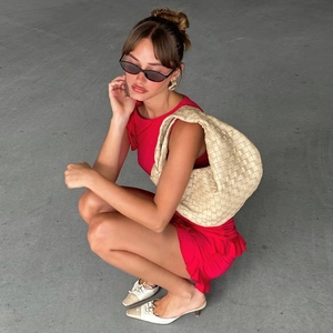 Dettaglio di una borsa hobo intrecciata beige abbinata a un abito corto rosso smanicato