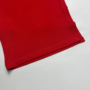 Detail shot of the red knitted T-shirt hem featuring dual-needle stitching and side slit