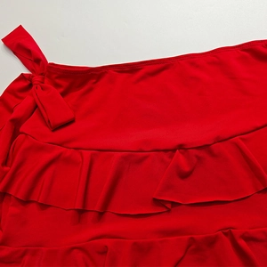 Dettaglio di minigonna rossa a balze con fiocco laterale in tessuto elastico lucido
