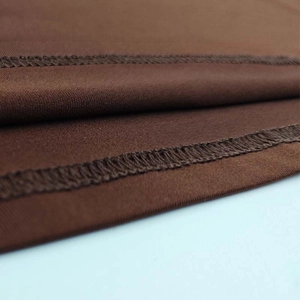 Detail of high-quality overlock stitching and seams on deep brown knitted stretch fabric