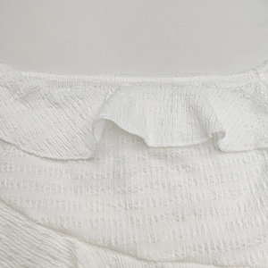 Détail du tissu texturé blanc avec col à volants et smocks sur cette robe élégante