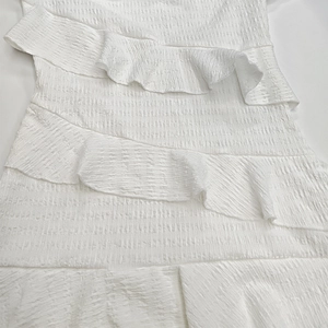 Détail de la robe blanche à épaules dénudées avec volants et texture de tissu plissé