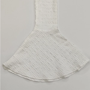 Détail de la robe blanche montrant le tissu smocké texturé et le bord de manche volanté