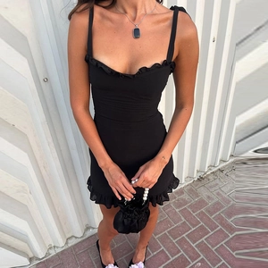 Detail of ruffle trim on a slim fit black mini dress with adjustable tie straps
