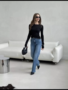 Detail of slim fit black long sleeve top styled with high waist frayed edge jeans