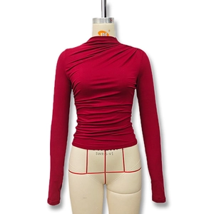 Detail of ruched red slim fit top featuring asymmetric pleated fabric and half high collar