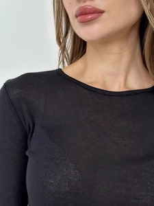 Detail of a sheer black long sleeve top showing the slim fit crew neck and knitted fabric