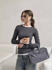 Close-up of dark grey slim top with layered white cuffs and matching suede handbag