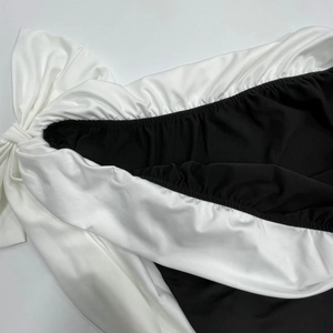 Détail de robe chic noire et blanche à épaules dénudées avec nœud et tissu froncé