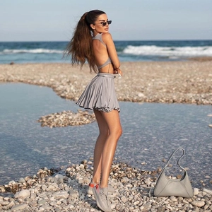 Detail of grey open back crop top and high waist pleated mini skirt set in outdoor setting