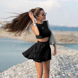 Chic black two-piece set featuring a backless crop top and high-waisted pleated mini skirt