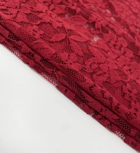 Detail of red floral lace fabric with intricate mesh cutouts and scalloped edges