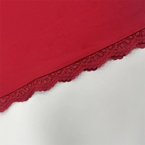 Detailed macro view of the delicate red lace trim and knit texture on the garment hem