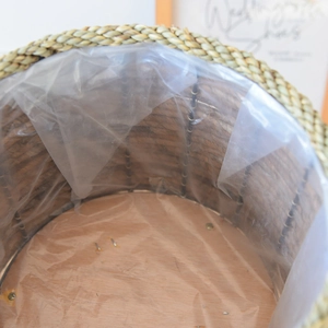 Detail showing natural woven planter with waterproof plastic liner and sturdy wooden base