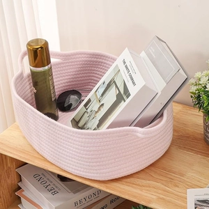 Pink woven cotton rope storage basket with handles showing books and skincare products