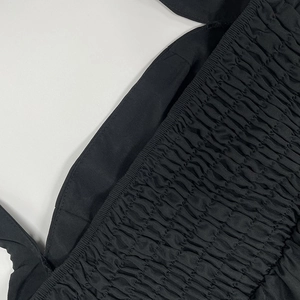 Detail eines schwarzen Kleides mit geraffter Textur und Schultergurten mit Rüschen