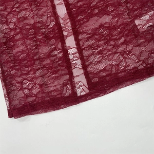 Dettaglio del tessuto in pizzo rosso vino con motivi floreali e trama a rete sul vestito
