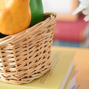 Macro detail of hand-woven wicker storage basket filled with decorative fruit on books