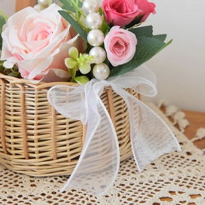 Detail of woven flower basket featuring pearl handle, pink roses and white lace bow