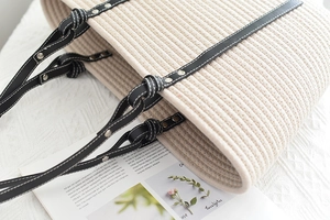 Close-up of woven cotton tote bag with black leather knotted handles and silver rivets