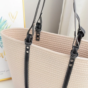 Detailed close-up of beige woven tote bag with black leather straps and silver rivets