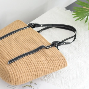 Close-up of woven tote bag texture with black leather strap and silver rivet detail