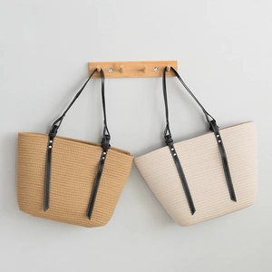 Close-up of woven straw tote bags with black leather straps and metal rivet details
