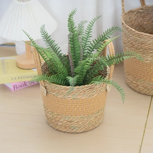 Detail of handmade woven plant basket with natural straw, gold silk accents and green fern