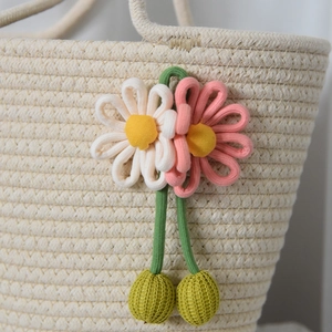 Dettaglio dei ciondoli floreali intrecciati rosa e bianchi su una borsa di paglia