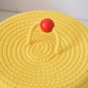 Detailed top view of a yellow woven storage basket lid with a red round wooden handle