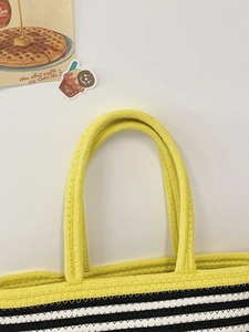 Close-up detail of yellow woven tote bag showing thick braided handles and striped patterns